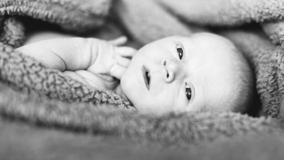 Schwarz-Weiß-Porträt eines Babys, das in eine Decke eingewickelt ist. © picture alliance/Bildagentur-online Foto: Jessica Peterson, Tetra-Images