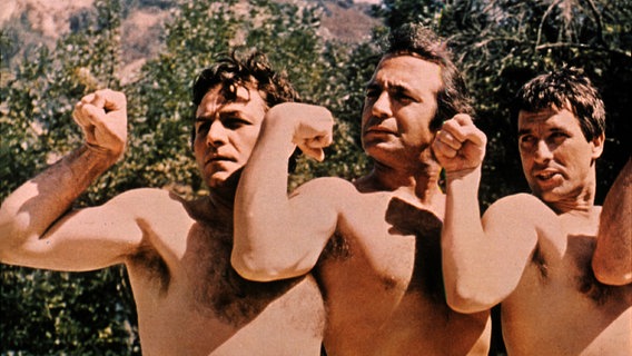 Zu sehen sind drei Männer mit nackten Oberkörpern nebeneinander, die ihre Muskeln zeigen. © picture alliance/United Archives Foto: United Archives/Impress
