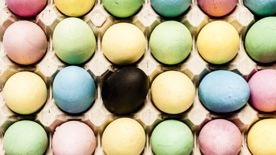 Zu sehen ist eine Palette bunter Eier von oben - in der Mitte ein schwarzes Ei. © imago / CHROMORANGE 