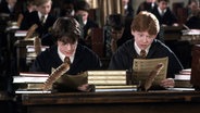 Eine Filmszene aus "Harry Potter und die Kammer des Schreckens": Harry und Ron sitzen im Klassenzimmer in Hogwarts. © picture alliance/United Archives Foto: United Archives/Impress