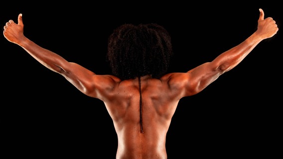Zu sehen ist der muskulöse Rücken eines Mannes. Seine Arme hat der Mann in einer Siegerpose nach oben gereckt und streckt beide Daumen in die Luft. © imago / blickwinkel 