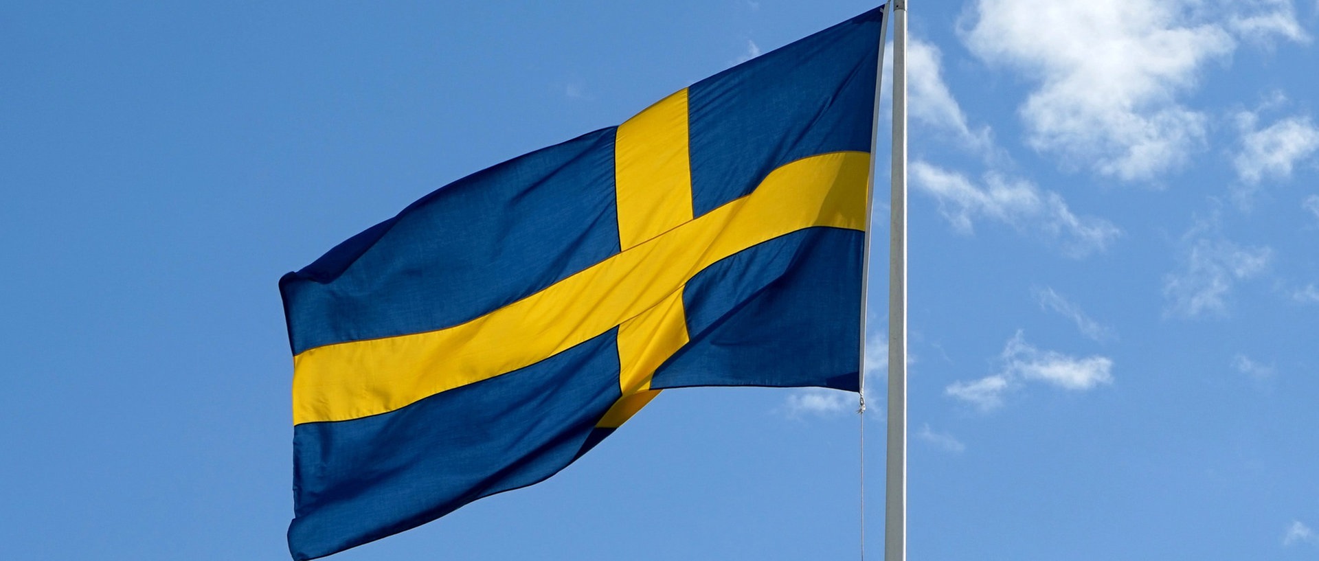 Die schwedische Nationalflagge weht an einem Mast im Wind., © picture alliance/dpaFoto: Daniel Kalker