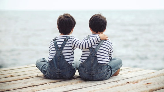 Zwei Jungs in gleichen Klamotten sitzen nebeneinander und sind von hinten zu sehen. © estherm / photocase.de Foto: estherm / photocase.de