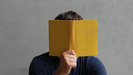 Jemand liest ein gelbes Buch und hält es vor sein Gesicht. © photocase.de / luxuz Foto: photocase.de / luxuz