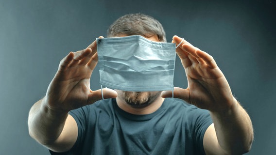Ein Mann hält sich eine Maske vor das Gesicht. © Brilliant Eye / photocase.de Foto: Brilliant Eye / photocase.de