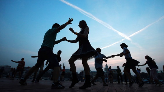 Mehrere junge Menschen tanzen in der Dämmerung im Freien. © picture alliance / dpa Foto: Sergei Fadeichev
