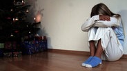 Ein Mädchen kauert traurig neben dem Weihnachtsbaum. © imago/emil umdorf Foto: emil umdorf