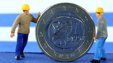 Zwei Miniaturfiguren stehen neben einer griechischen Euromünze © dpa 