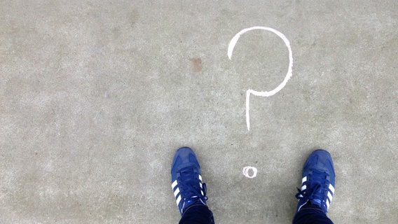 Ein auf ein Stein gemaltes Fragezeichen wir dvon zwei Sneakern flankiert. © NDR Foto: Pascal Strehler