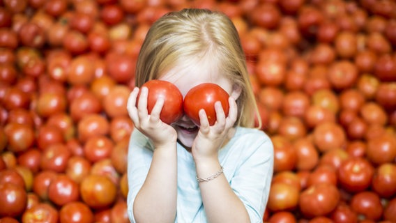 Ein Mädchen hält sich zwei Tomaten vor die Augen. © imago images/Westend61 Foto: Westend61