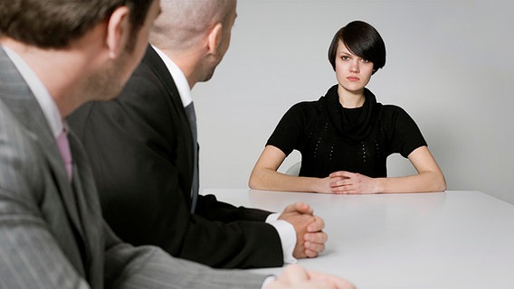 Junge Frau sitzt mit ernstem Blick zwei Männern im Büro gegenüber © picture-alliance / beyond/diffus Foto: beyond/diffused