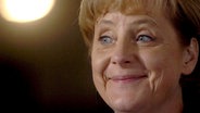 Angela Merkel grinst. Im Hintergrund ein Lichtkegel. © dpa Picture Alliance 