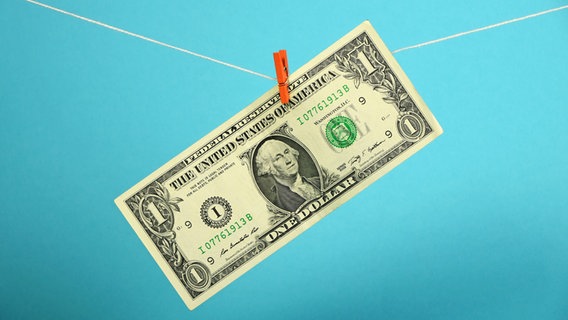 Eine 1-Dollar-Note hängt mit einer Wäscheklammer auf einer Wäscheleine.  
