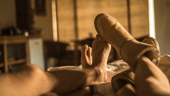 Zu sehen sind vier Füße eines Paares im Bett. Die Frau trägt dicke Hausschuhe. © Goulden / photocase.de Foto: Goulden