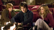 Daniel Radcliffe als Harry Potter, Rupert Grint als sein bester Freund Ron und Emma Watson als Bücherwurm Hermine in einer Szene aus dem Film "Harry Potter und der Feuerkelch": Die drei sitzen auf einem Sofa und starren auf ein Feuer. © dpa - Bildfunk Foto: dpa-Film Warner