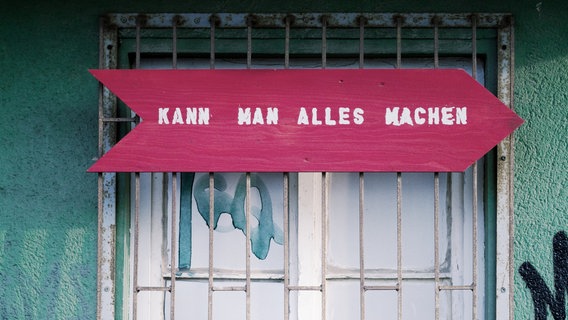 Zu sehen ist ein Fenster, vor dem ein pinkes Schild hängt. Darauf steht: "Kann man alles machen." © ginger. / photocase.de Foto: ginger.