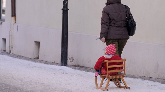 Ein kleines Mädchen wird auf einem Holzschlitten von einer Erziehungsberechtigten gezogen. © imago/Ulmer 