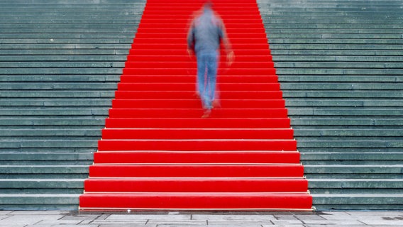 Ein Mensch geht eine Treppe hoch, die mit rotem Teppich ausgelegt ist. © kallejipp / photocase.de Foto: kallejipp
