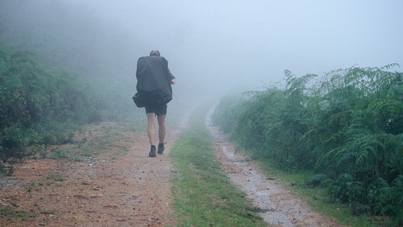 Zu sehen ist ein Mann mit Rucksack, der durch eine nebelige Landschaft wandert. © picapau / photocase.de Foto: picapau