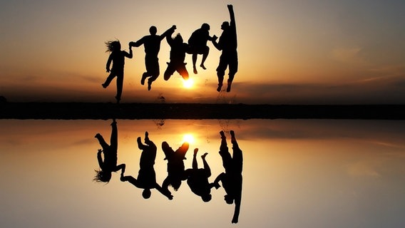 Fünf Jugendliche springen am Strand dem Sonnenuntergang entgegen. © Photocase Foto: Emanoo