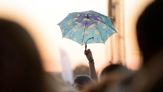 Ein Mann hält auf dem Dockville Festival 2012 einen Regenschirm in die Luft. © NDR / fotografirma Foto: Benjamin Hüllenkremer