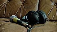 Ein Mikrofon und Kopfhörer liegen auf einem braunen Ledersofa. © Photocase Foto: Alwayshappy