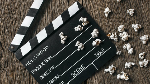 Das Bild zeigt eine Filmklappe, die auf einem Holztisch mit Popcorn liegt. © imago / westend61 Foto: westend61