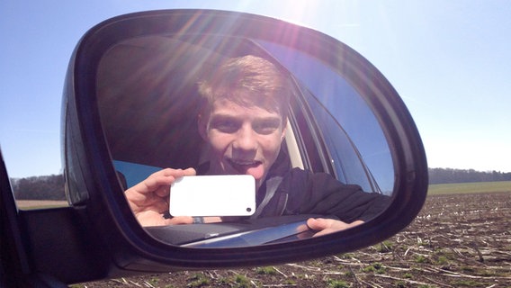 Ein junger Mann schaut in den Außenspiegel eines Autos und macht ein Selfie. © fotolia Foto: grafikplusfoto