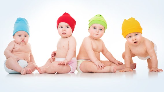 Vier Babys mit farbigen Mützen sitzen nebeneinander. © Fotolia Foto: Svetlana Fedoseeva