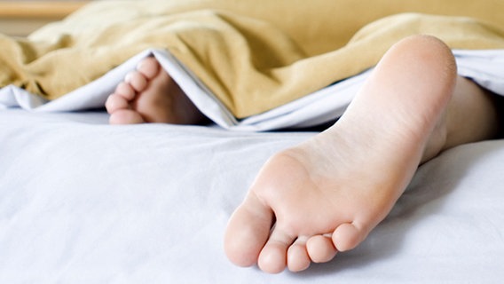 Nackter Fuß guckt unter einer Bettdecke hervor. © Fotolia.com Foto: Alexey Stiop