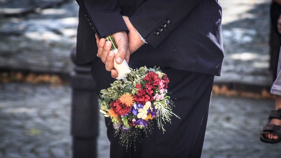 Ein Mann im Anzug hält einen Blumenstrauß hinter seinem Rücken in beiden Händen fest. © photocase.de / David Dieschburg Foto: photocase.de / David Dieschburg