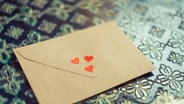 Ein Brief mit drei kleinen Herzchen liegt auf einem Tisch. © Eliza / photocase.de Foto: Eliza / photocase.de