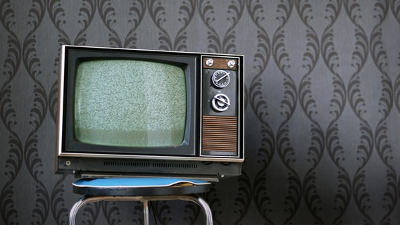 Ein alter Fernseher steht auf einem Hocker vor grauer Tapete. © photocase.de / complize Foto: photocase.de / complize