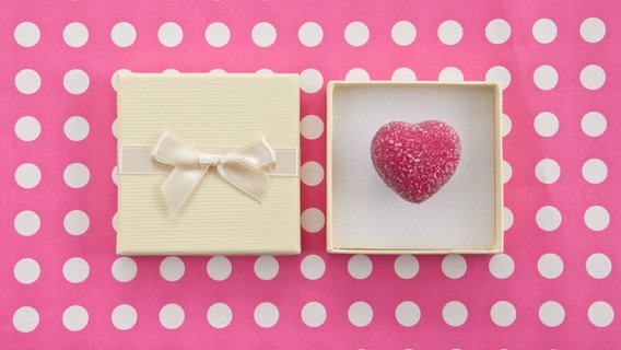 Eine Schachtel mit einem Herz drin liegt auf einer pinken Tischdecke. © imago/CHROMORANGE Foto: CHROMORANGE