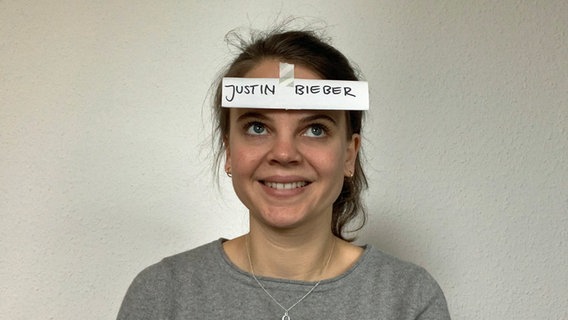 Ein Spiel: Eine Frau hat für "Wer bin ich?" einen Zettel mit dem Namen Justin Bieber auf der Stirn kleben. © NDR/N-JOY 