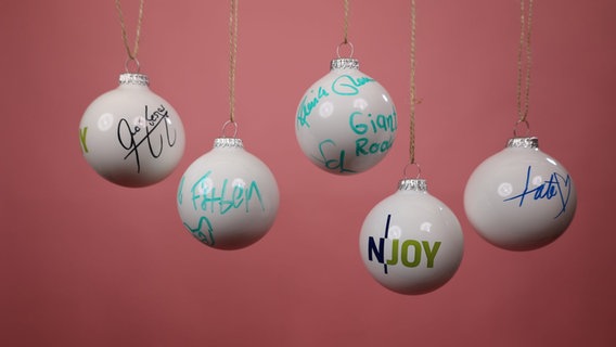 Von Stars signierte N-JOY Weihnachtskugeln vor einem rosa Hintergrund. © NDR/N-JOY Foto: NDR/N-JOY