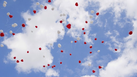 Am Himmel fliegen viele rote und weiße Luftballons in Herzchenform. © imago/Westend61 Foto: Westend61