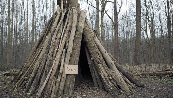 In einem Wald steht eine Hütte aus Baumstämmen. Daran hängt ein Schild mit der Aufschrift "For rent". © imago/Westend61 Foto: Westend61