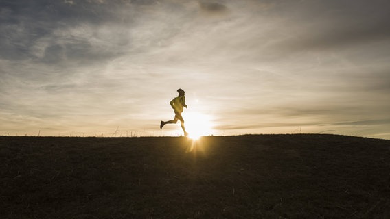 Ein Mann läuft im Sonnenuntergang. © imago/Westend61 Foto: Westend61