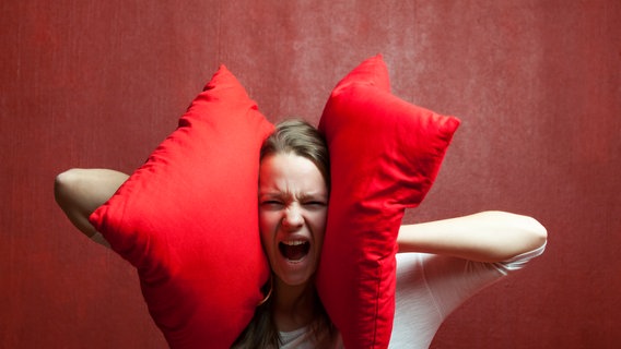 Eine Frau schreit und hält sich die Ohren mit roten Kissen zu. © bernjuer / photocase.de Foto: bernjuer / photocase.de