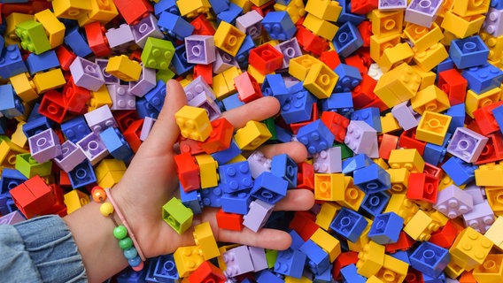 Ein Kind greift mit einer Hand in eine Kiste mit bunten Lego-Steinen. © picture alliance/Patrick Pleul/dpa-Zentralbild/ZB Foto: Patrick Pleul