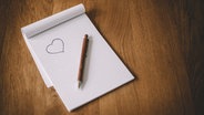 Ein Block mit einem gemalten Herz, auf dem Blatt liegt ein Stift. © tobid / photocase.de Foto: tobid / photocase.de