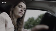 Screenshot aus einem Video zur Aktion "Kopf hoch. Das Handy kann warten": Linda Zervakis sitzt am Steuer eines Autos und schaut aufs Handy. © NDR / N-JOY 