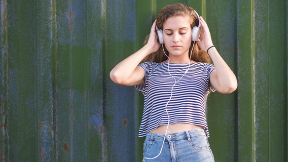 Eine junge Frau in Hotpants hört Musik über Kopfhörer. © imago/Westend61 