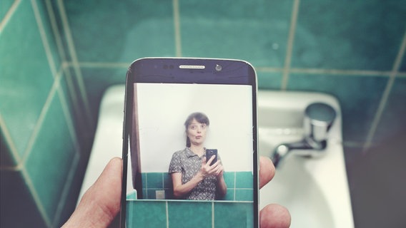 Eine Frau hält vor einem Waschbecken ein Smartphone, das ein Selfie zeigt. © Andeera / photocase.de Foto: Andeera / photocase.de