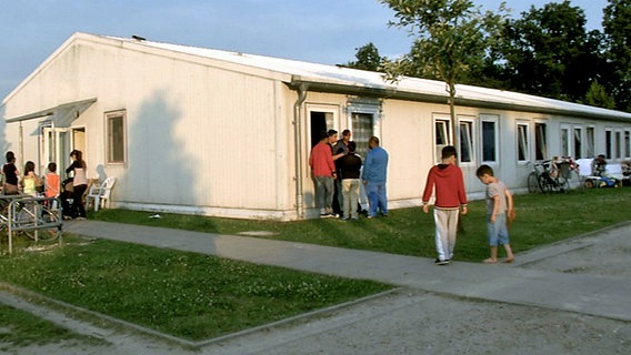 Asylbewerberheim mit Bewohnern davor.  