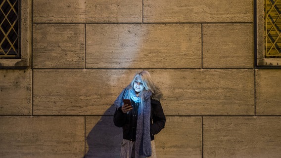 Eine Frau steht an einer Hauswand und schaut auf ihr Handy. © imago/Westend61 Foto: Westend61