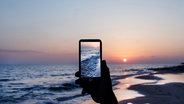 Jemand macht mit dem Smartphone ein Foto vom Sonnenuntergang. © katrinshine / photocase.de Foto: katrinshine / photocase.de