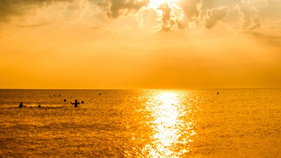 Die untergehende Sonne spiegelt sich im Meer, in dem Menschen schwimmen. © photocase.de / jdirmeitis Foto: photocase.de / jdirmeitis