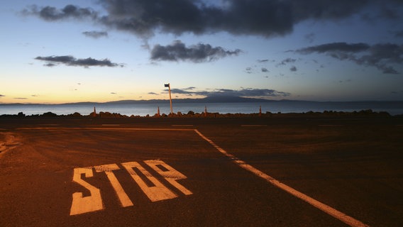 Zu sehen ist ein Parkplatz am Meer. Auf dem Boden steht "STOP". © imago/Westend61 Foto: Westend61